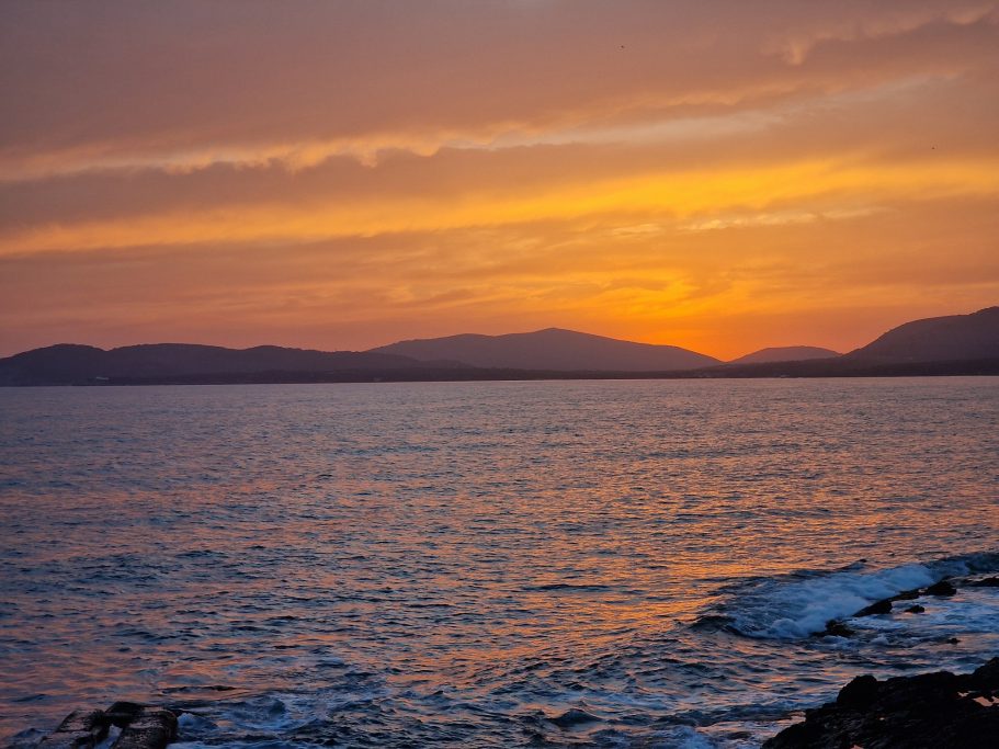 Sonnenuntergangsstimmung Sonnenuntergang über dem Meer mit sanften Wellen und silhouettierten Bergen im Hintergrund